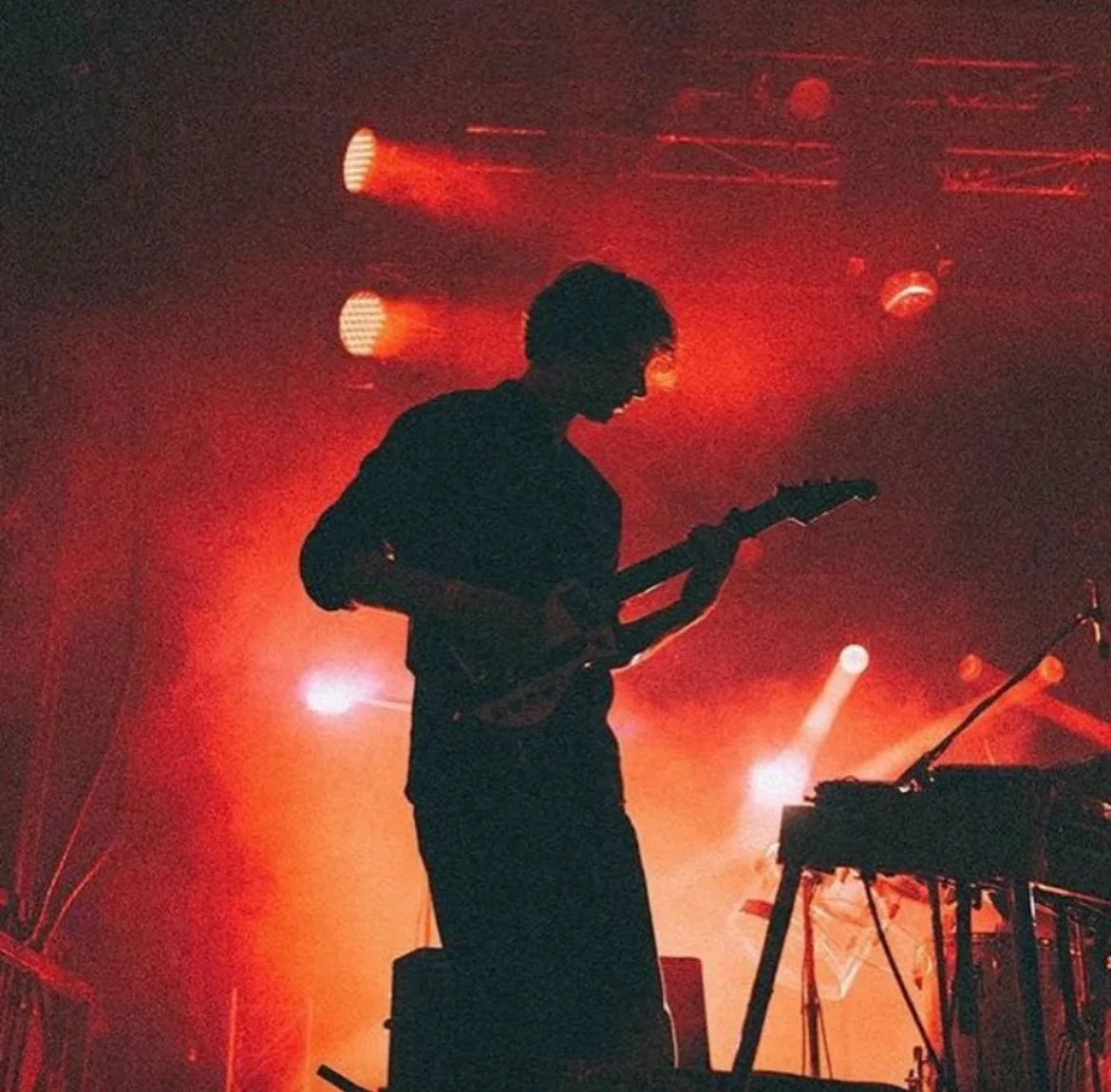 Brett in silhouette playing guitar under red stage lights