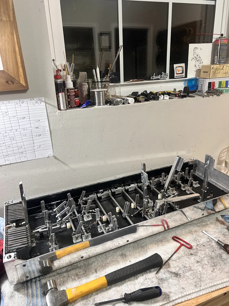 A pedal steel's mechanism on the bench, with its copedent chart taped to the wall above