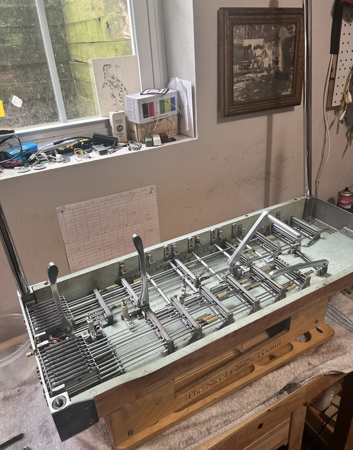 A pedal steel with a green felt underside, turned over on the bench under the window