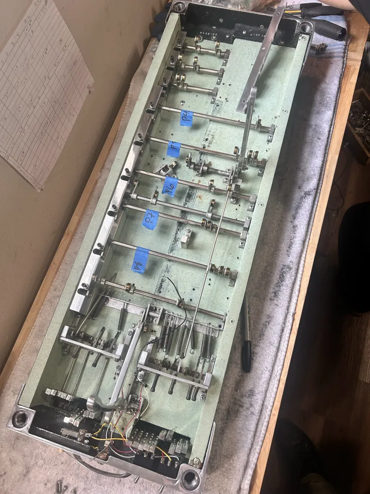 A pedal steel opened up on green felt, its pull rods labelled with blue tape
