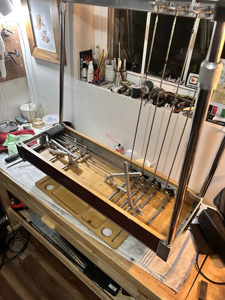A pedal steel upside down on the bench with its pedal rods attached and the mechanism showing