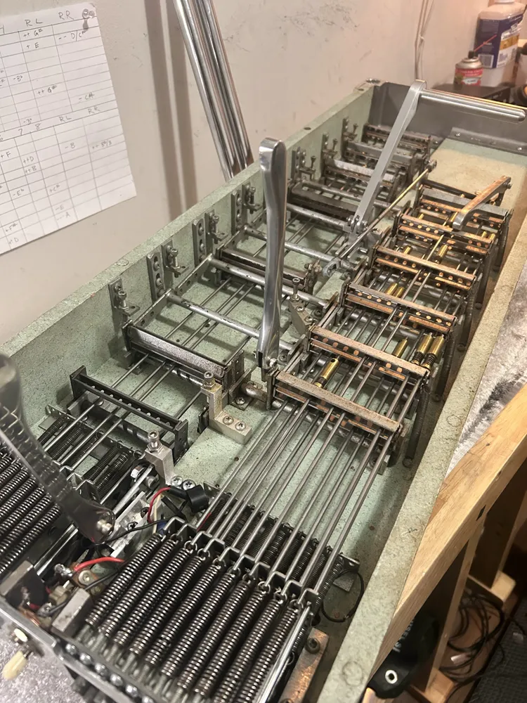 A pedal steel turned over: rows of return springs, pull rods and bell cranks on green felt