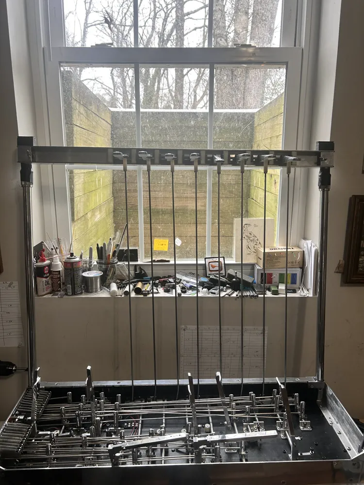 A pedal steel upside down under the workshop window, its pedal rods hanging from the rack