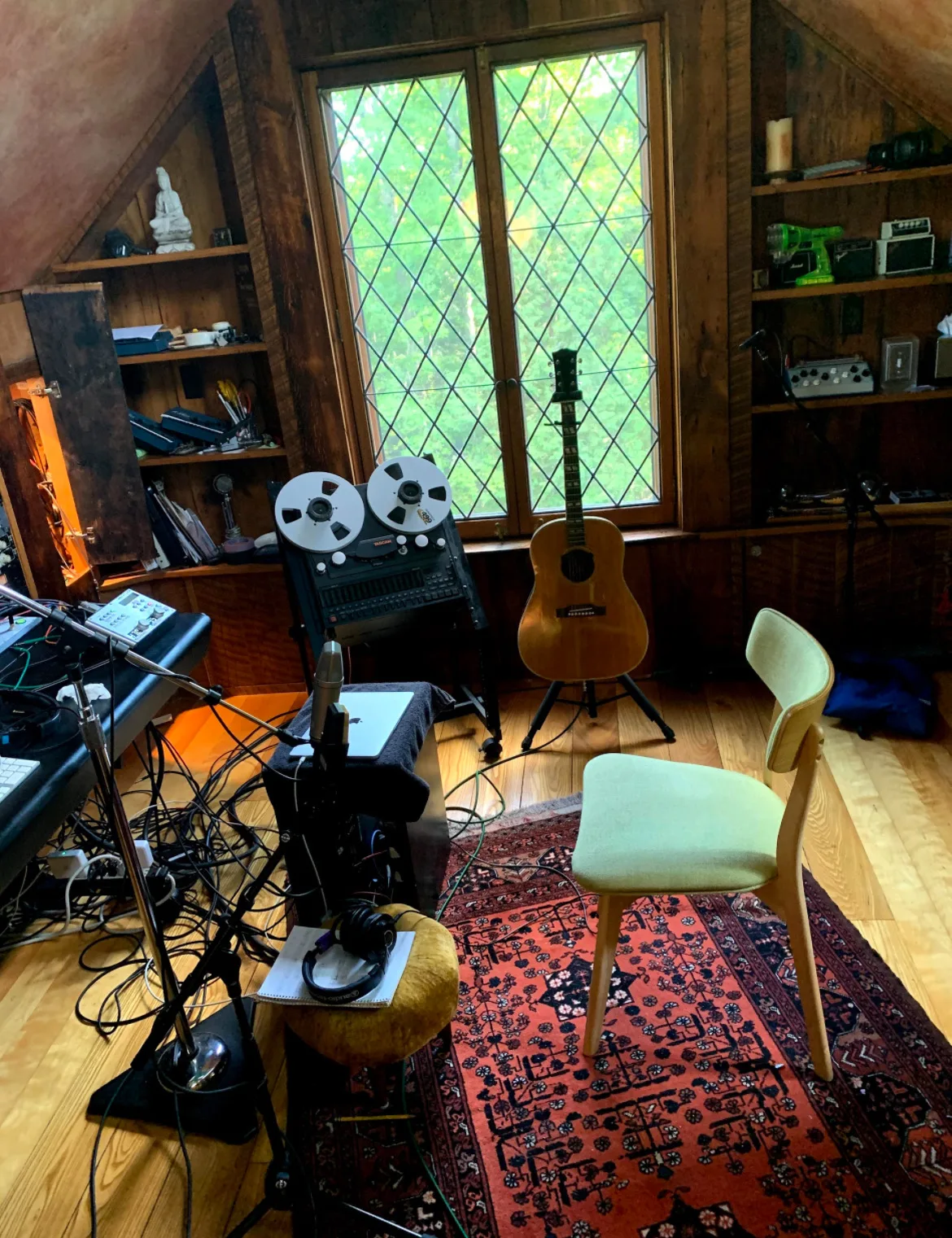The attic studio: a tape machine, an acoustic guitar and a chair on a red rug under a leaded window