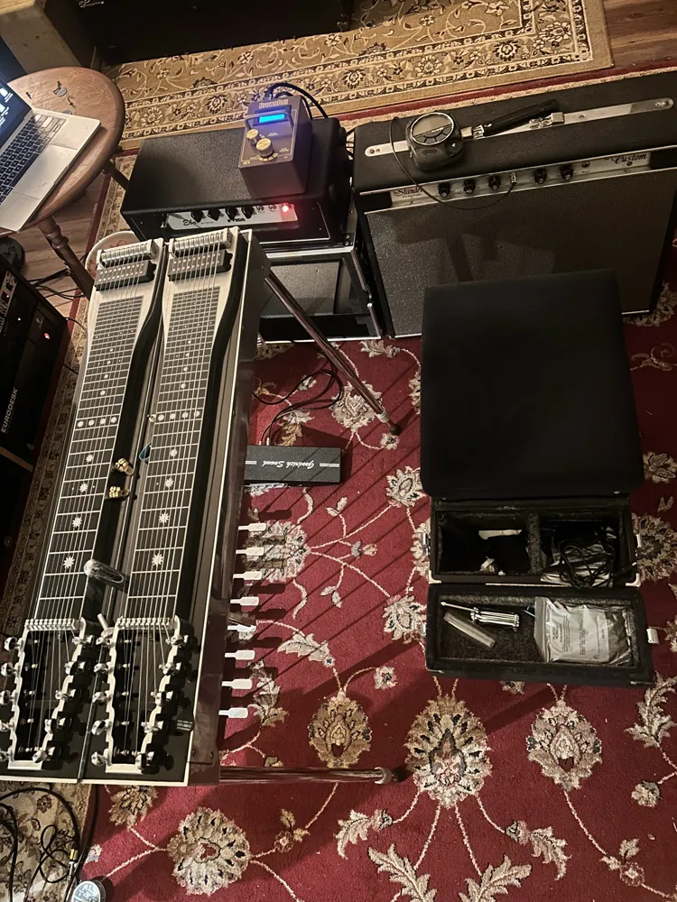 A double-neck pedal steel set up on a rug with two amps and a pedal, ready to track